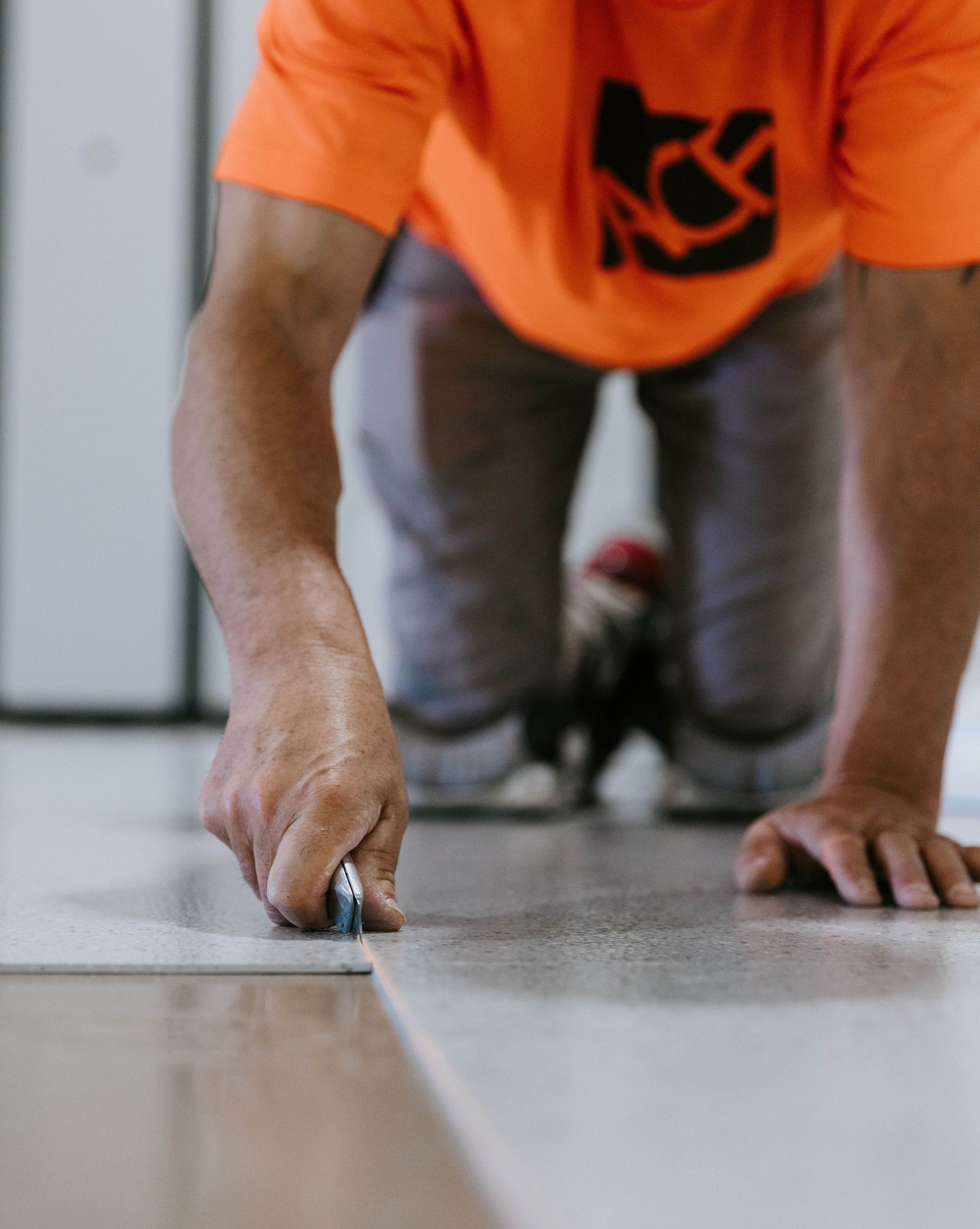 A man in an orange shirt is measuring a piece of wood with a tape measure.