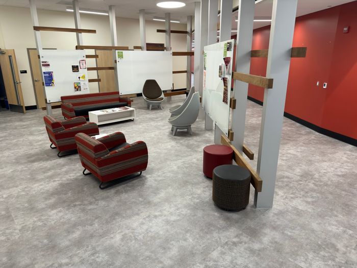 A room with a couch, chairs, ottomans and a whiteboard.