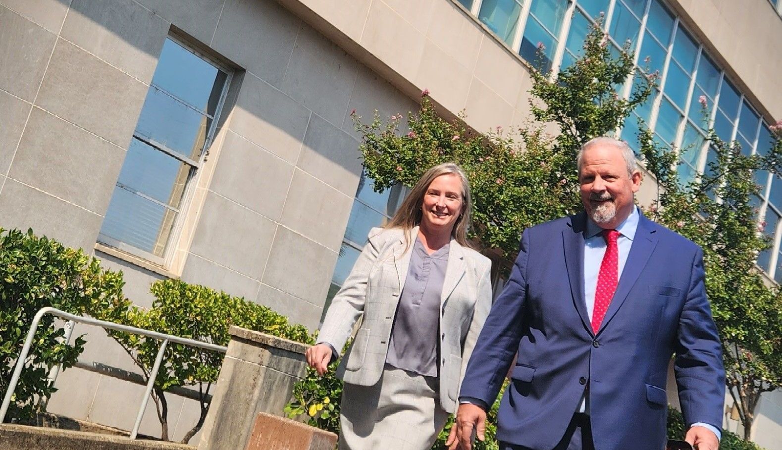 A man and a woman are walking in front of a building.