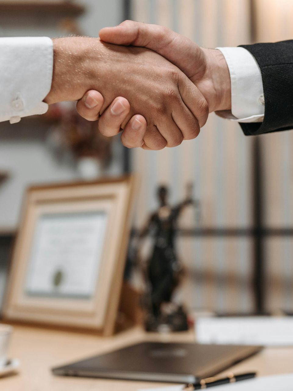Two men are shaking hands in front of a statue of justice.