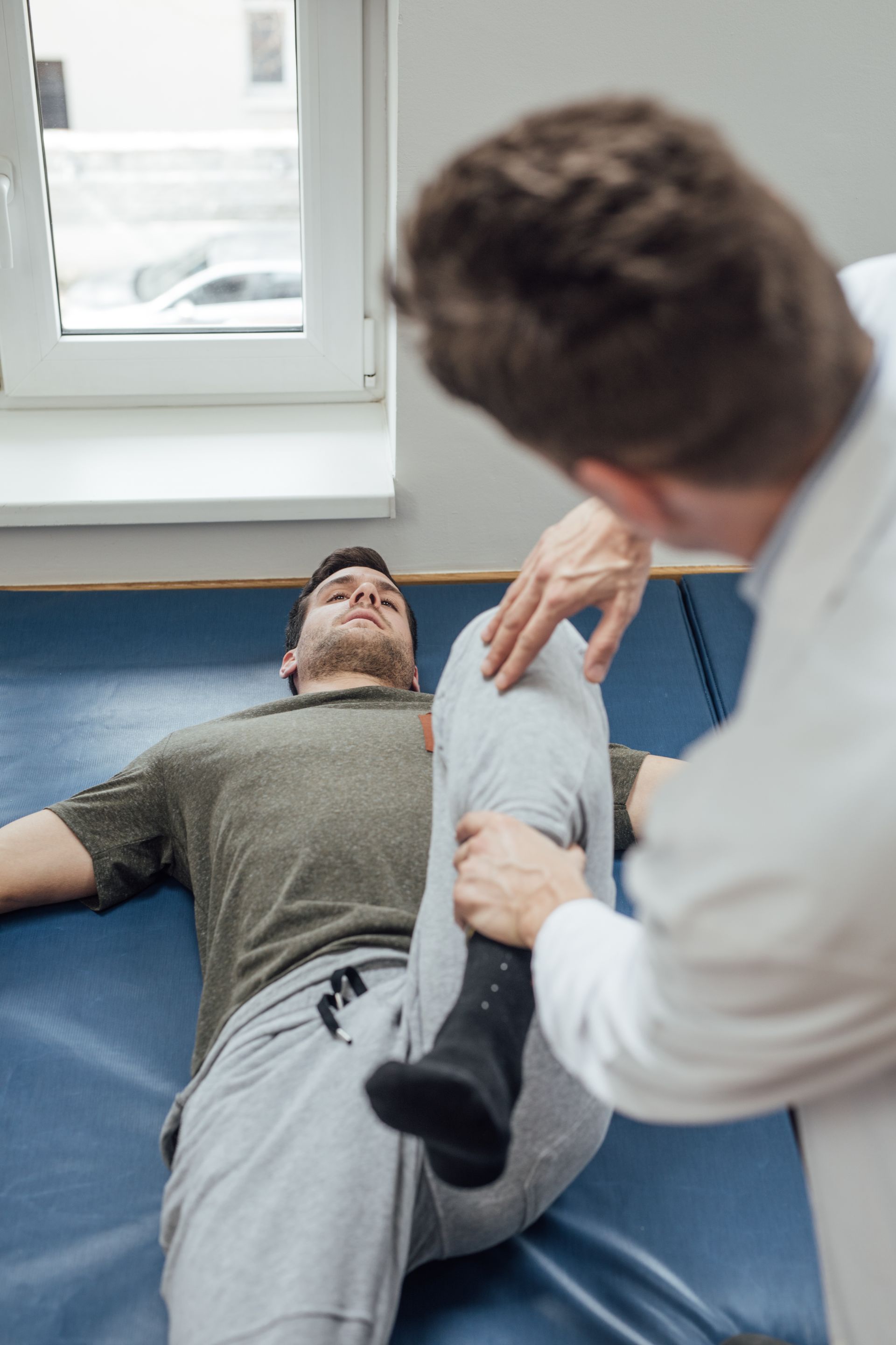 Physical therapist stretching a patient’s leg on a blue mat in a clinic. Physical therapist stretching a patient’s leg on a blue mat in a clinic.
