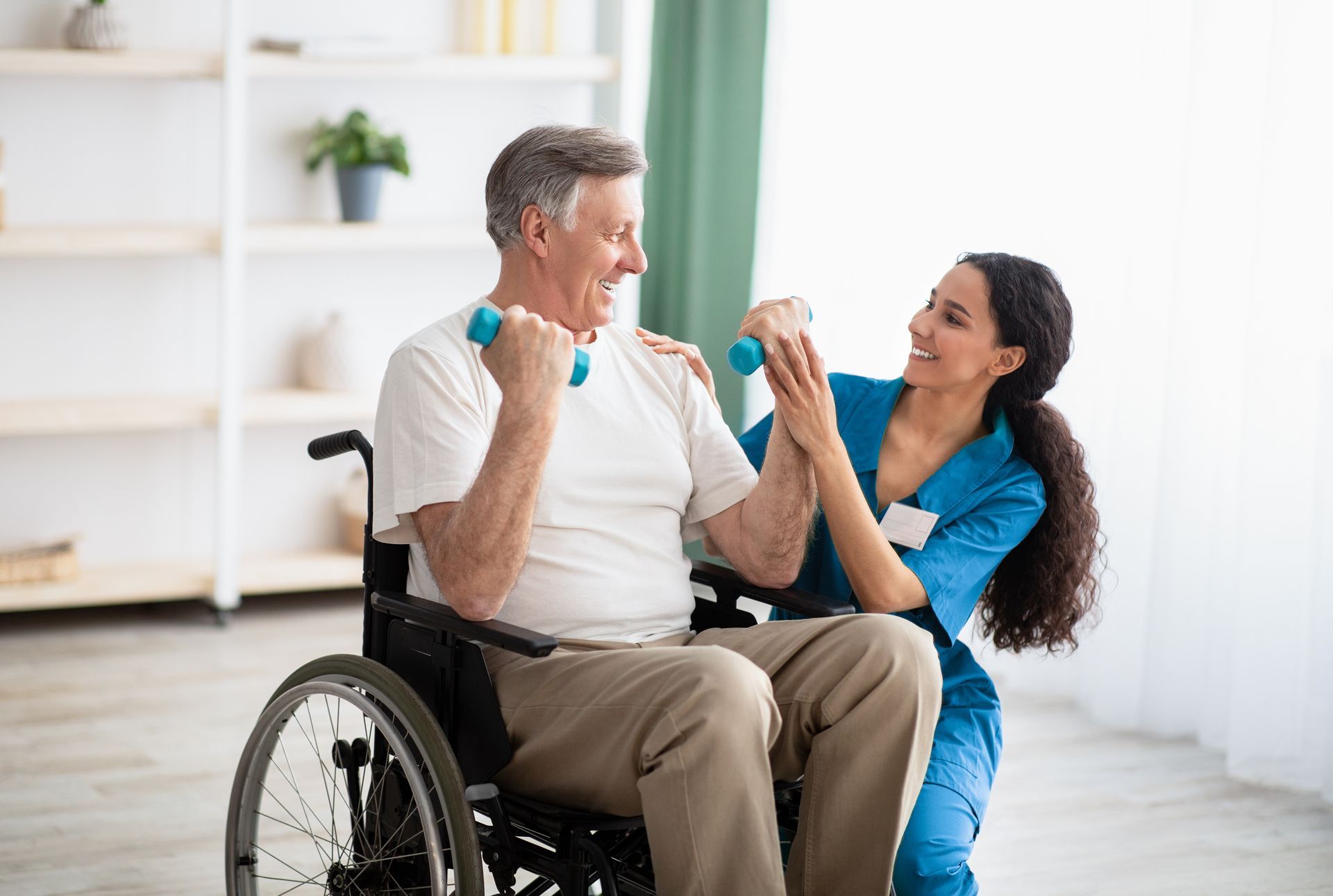 Person in wheelchair exercises with a trainer using blue dumbbells in a bright room Person in wheelchair exercises with a trainer using blue dumbbells in a bright room