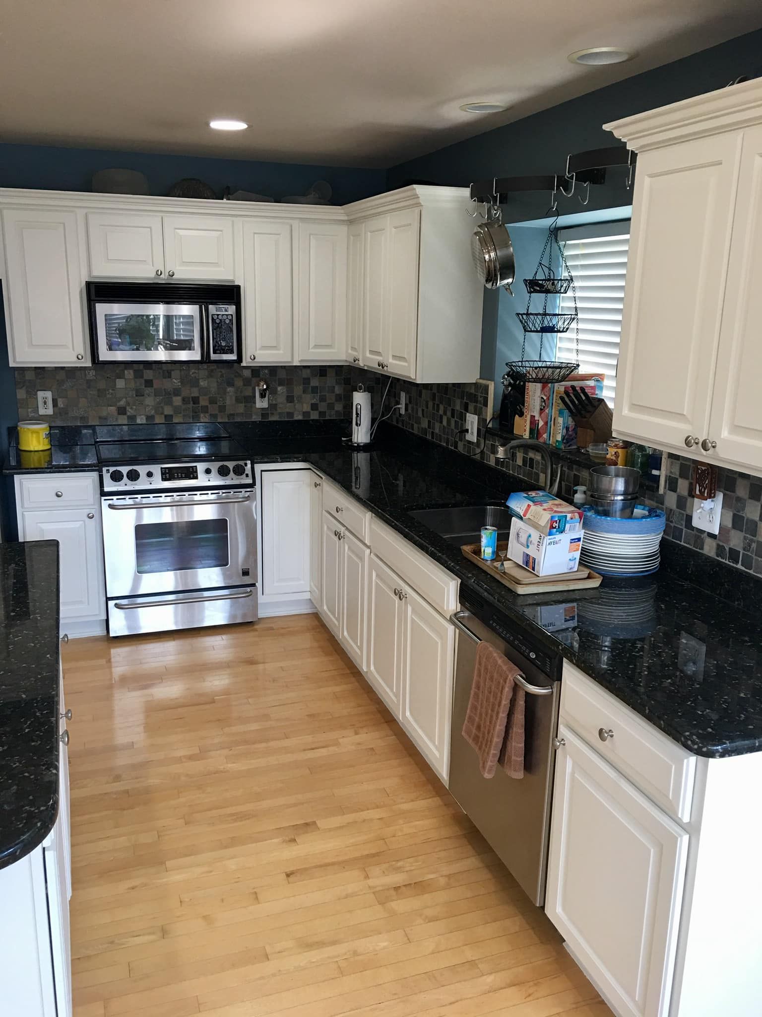 A modern kitchen with white cabinets, black granite countertops, stainless steel appliances, and light wood flooring.