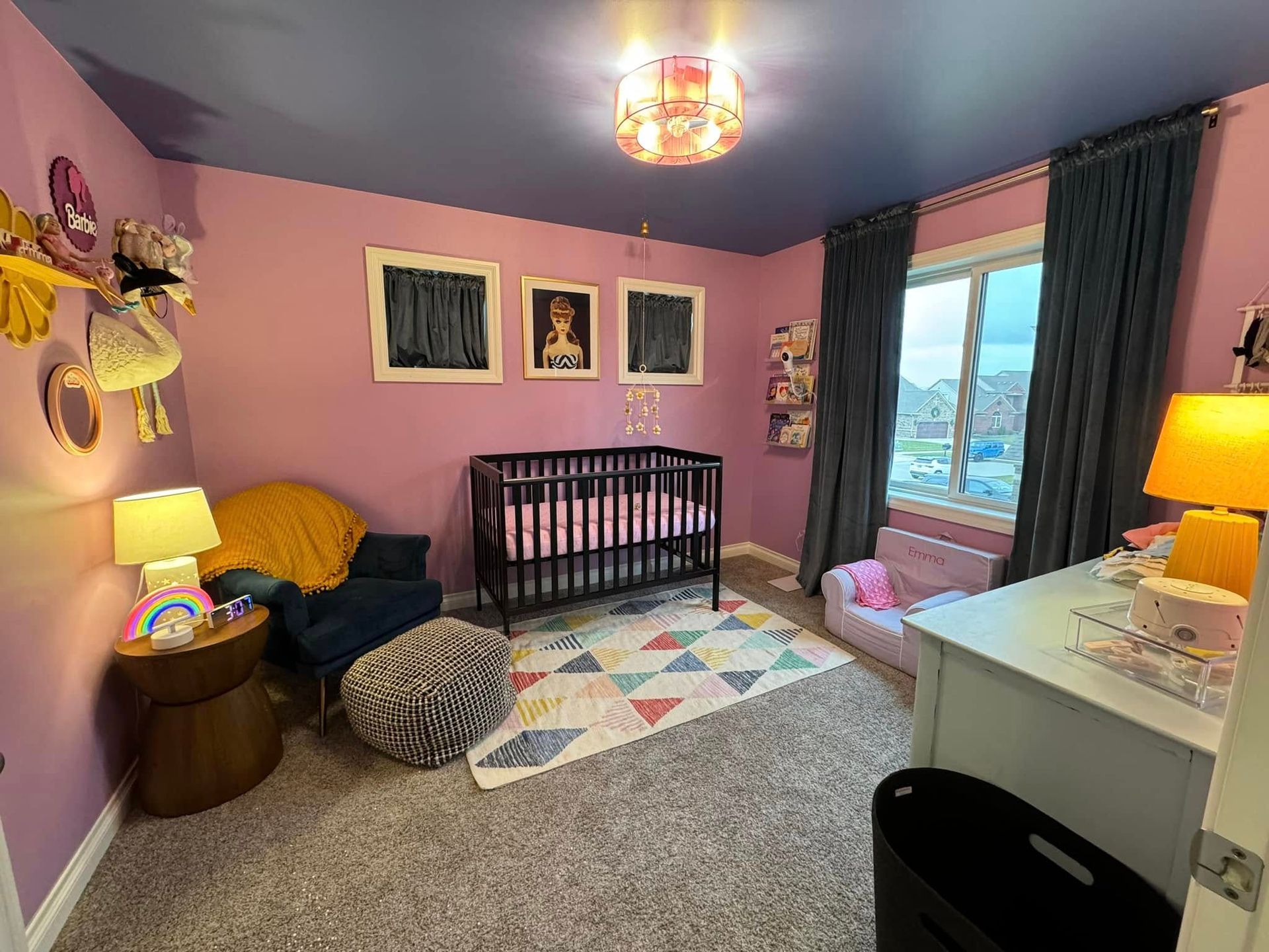 A nursery with lavender walls, a dark ceiling, a crib, a blue armchair with a yellow blanket, and a geometric rug.