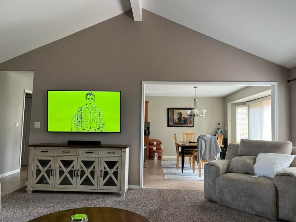 A wall-mounted TV displaying a green image sits above a white wooden media console in a living room near a dining area.