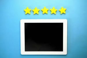A white tablet with a blank black screen positioned below five yellow stars against a solid blue background.