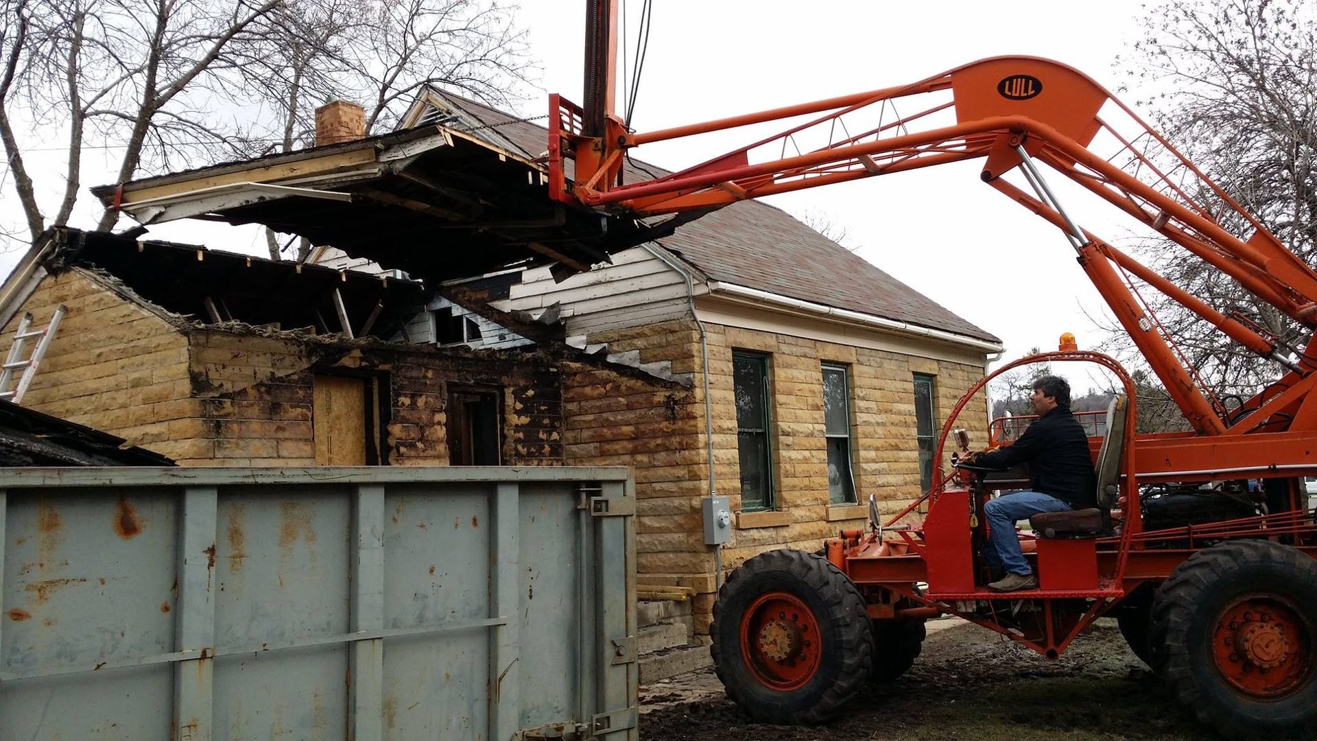 A man is driving an orange forklift in front of a house