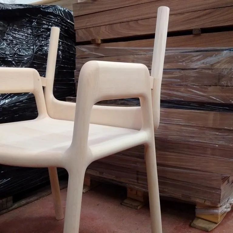 In un magazzino, due sedie bianche sono impilate davanti a pallet di legno imballati.