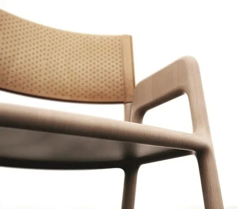 Primo piano di una sedia in legno color cuoio con schienale e braccioli perforati su sfondo bianco.