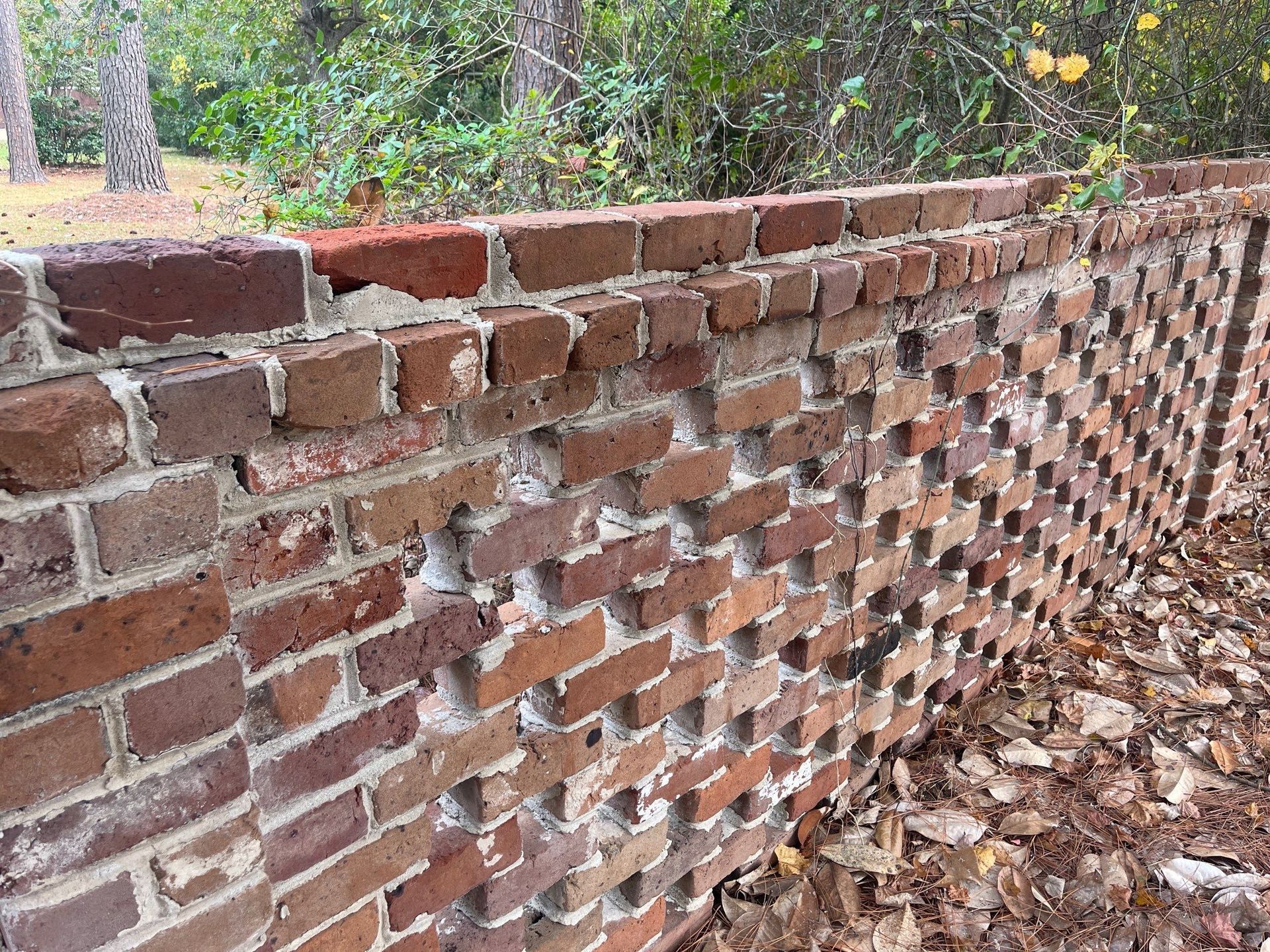 A brick wall with holes in it is surrounded by trees and leaves.