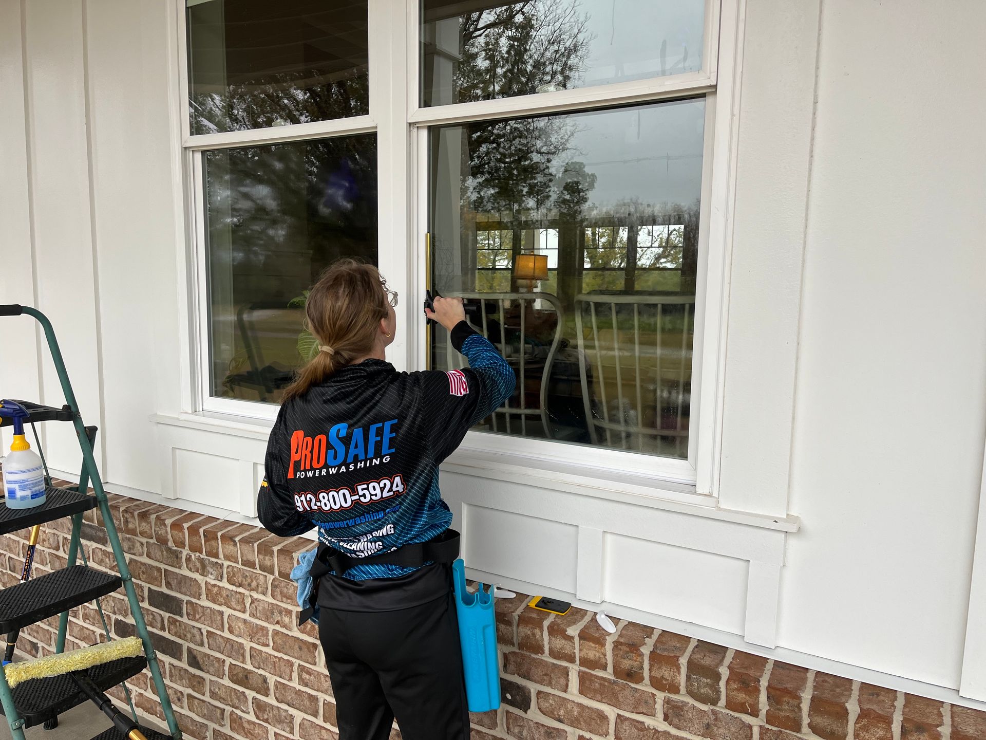 a woman wearing a prosafe shirt is cleaning a window