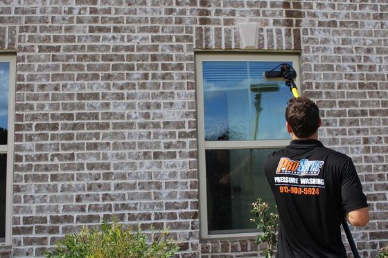 Man washing windows on a two-story house with a long-handled tool under a blue sky.