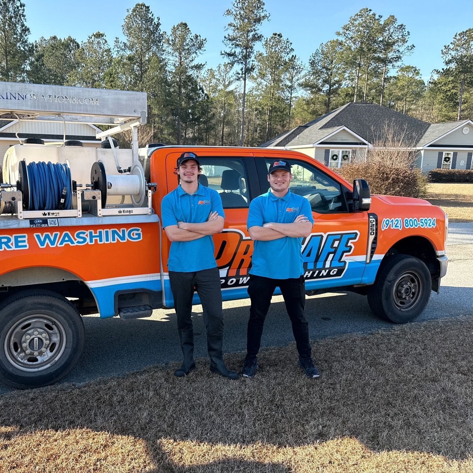 Two people stand with arms crossed in front of an orange and blue ProSafe power washing truck parked in a residential area.