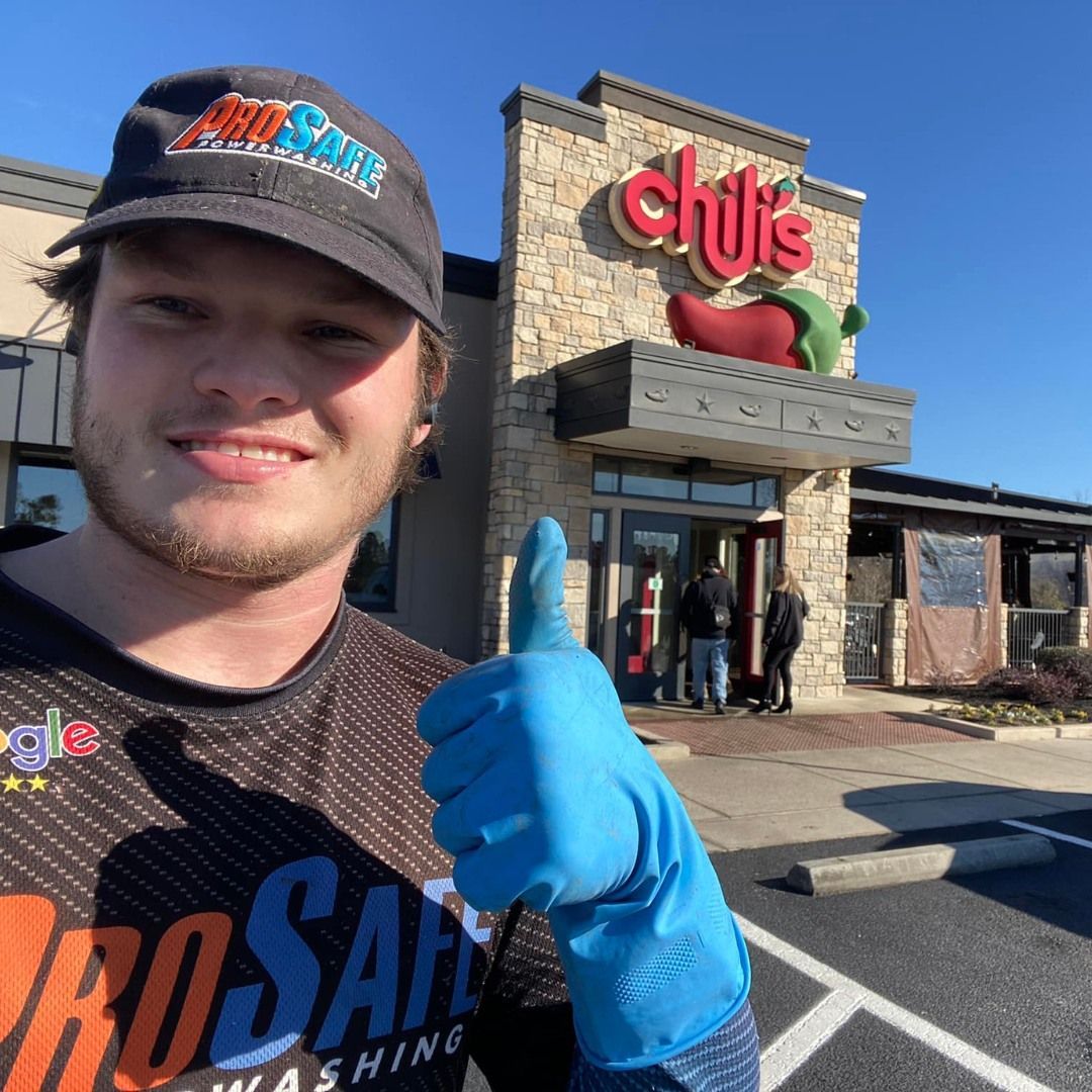 A person wearing a ProSafe uniform and blue cleaning glove gives a thumbs up in front of a Chili's restaurant exterior.