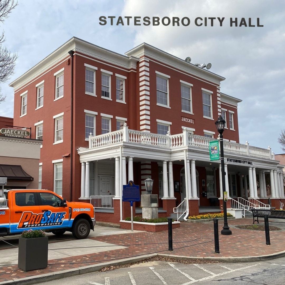 The red brick Statesboro City Hall building features a white porch and columns, with an orange truck parked out front.