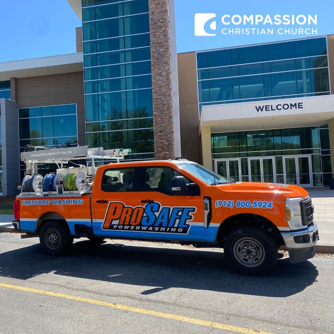 An orange ProSafe Power Washing truck parked in front of Compassion Christian Church under a clear blue sky.