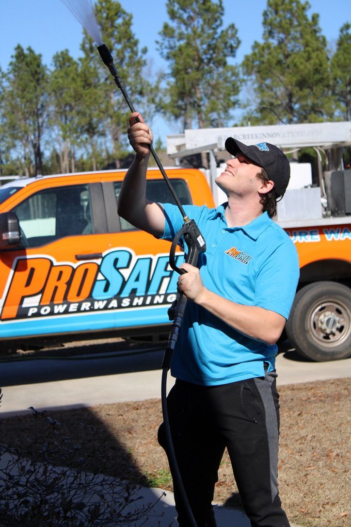 A worker in a blue polo shirt using a power washer, with a ProSafe branded truck in the background.