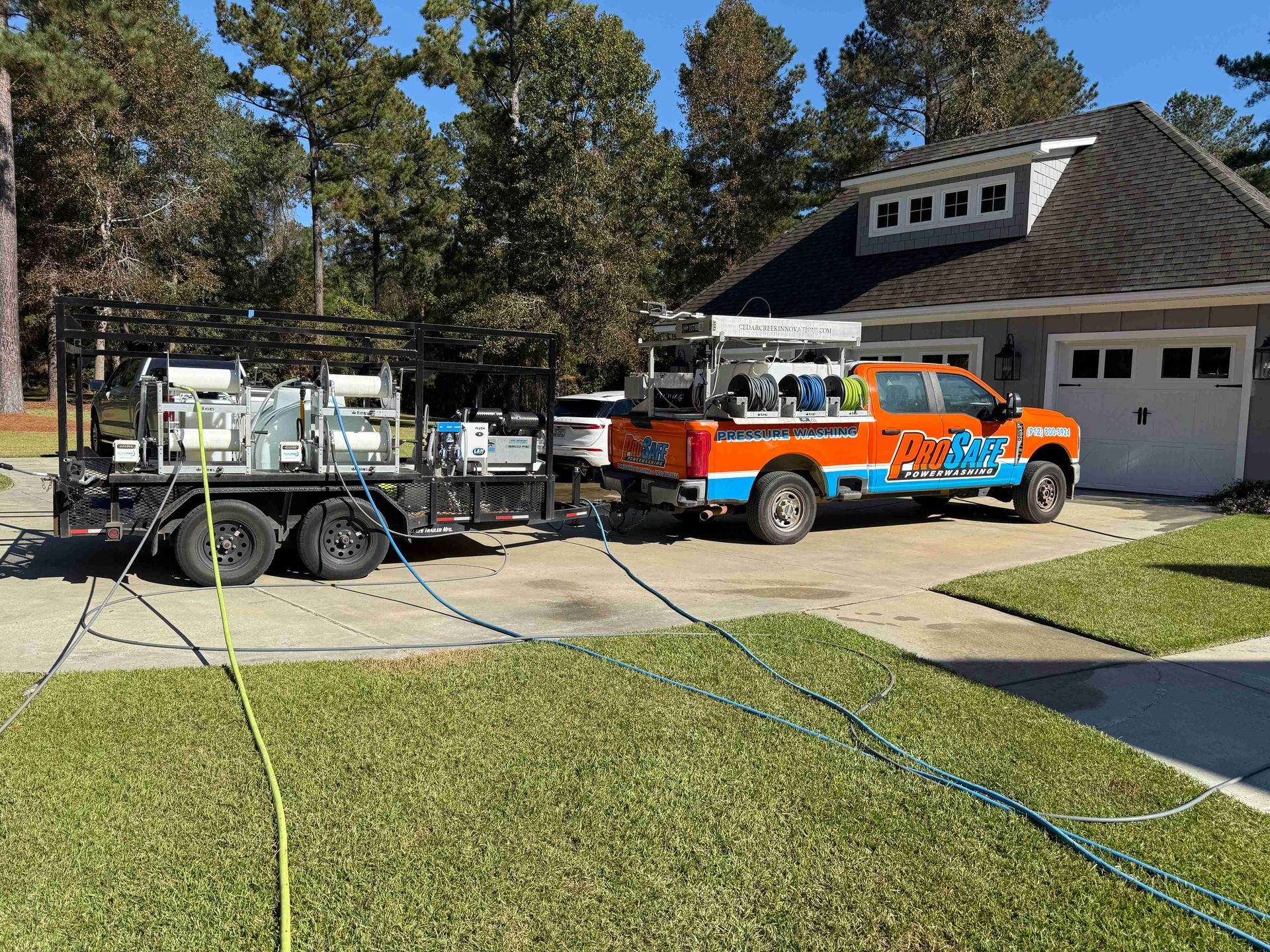 An orange and blue service truck with a utility trailer parked in a residential driveway on a sunny day.