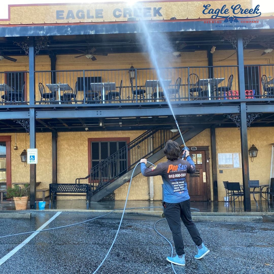 A worker in a blue shirt uses a pressure washer to clean the exterior of the Eagle Creek restaurant building.