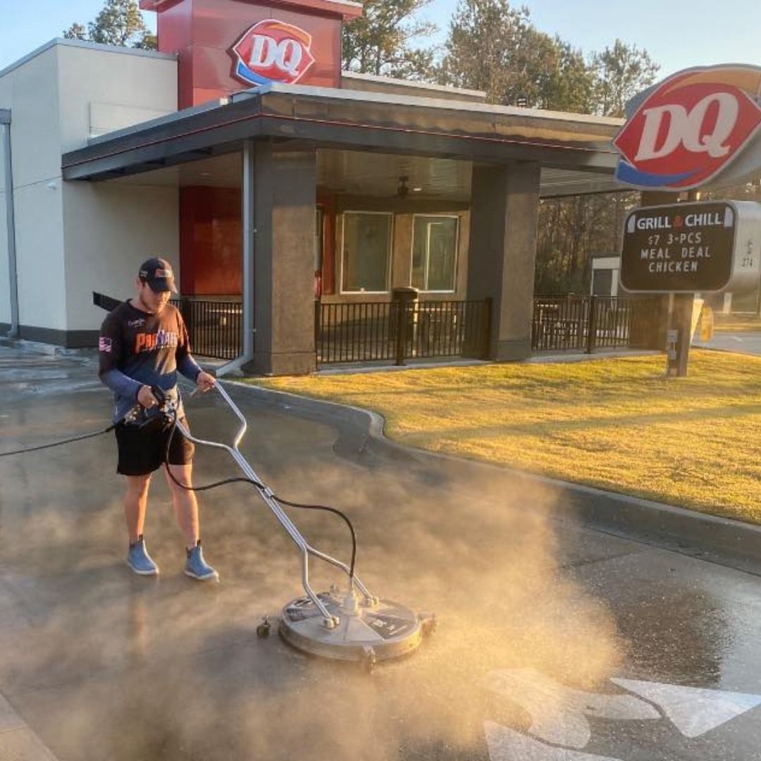 A person using a circular power washer to clean the concrete drive-thru area of a Dairy Queen restaurant.
