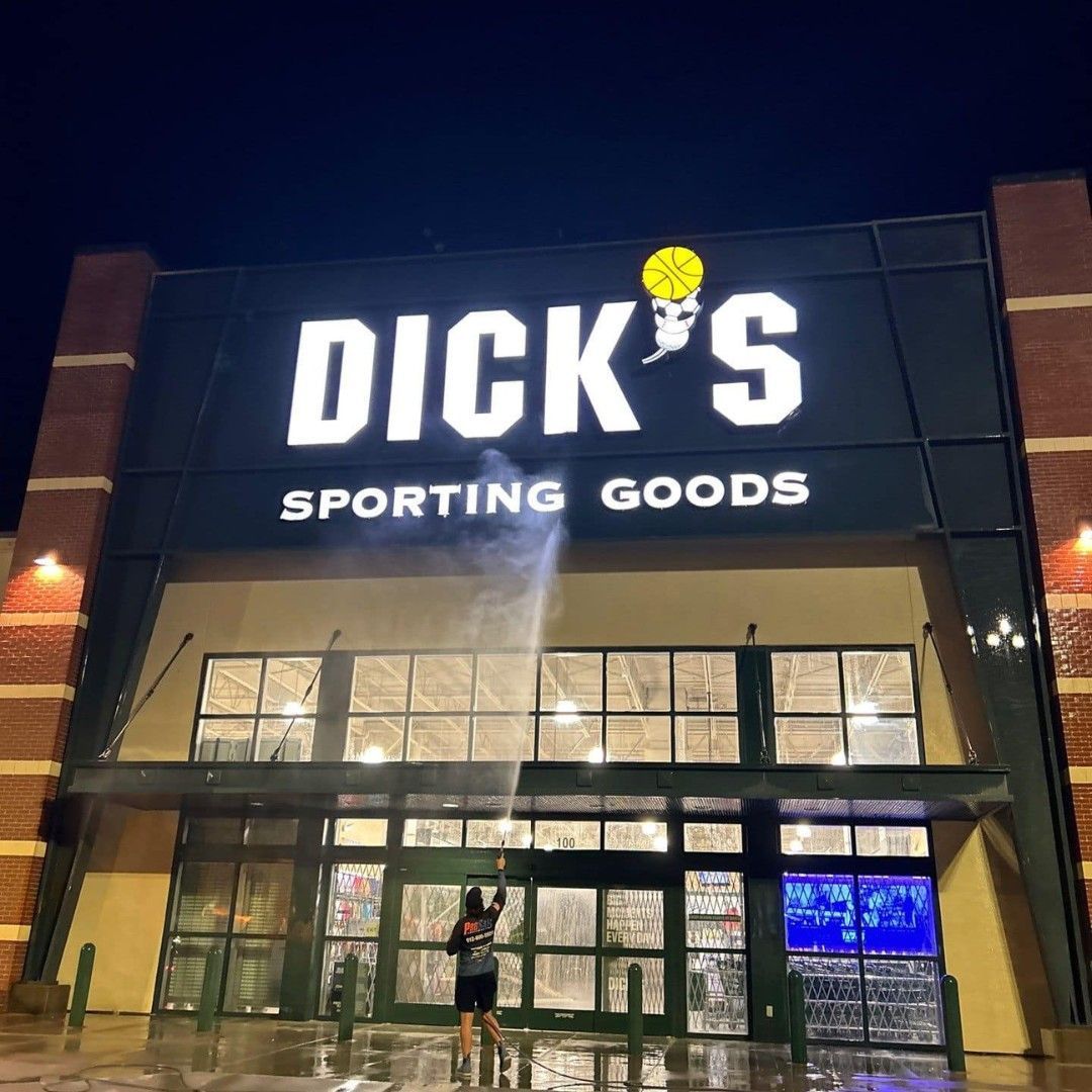 A person stands in front of a Dick's Sporting Goods store at night, holding a sparkler that emits light against the facade.