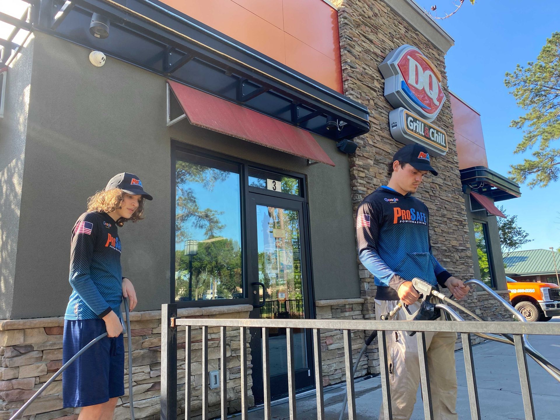Two people in matching blue fishing jerseys use pressure washers to clean the exterior of a Dairy Queen restaurant.