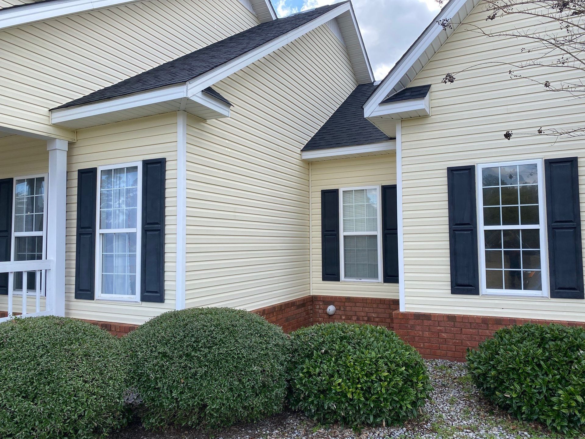 A yellow house with black shutters and bushes in front of it.