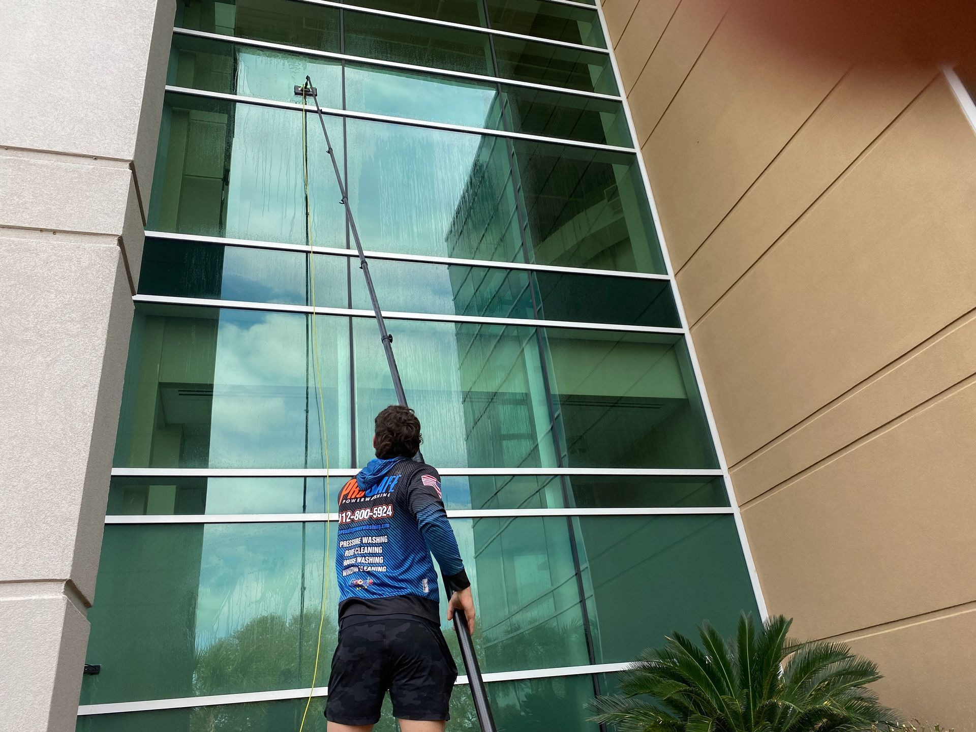A professional window cleaner uses an extended pole to clean the exterior glass of a modern building.