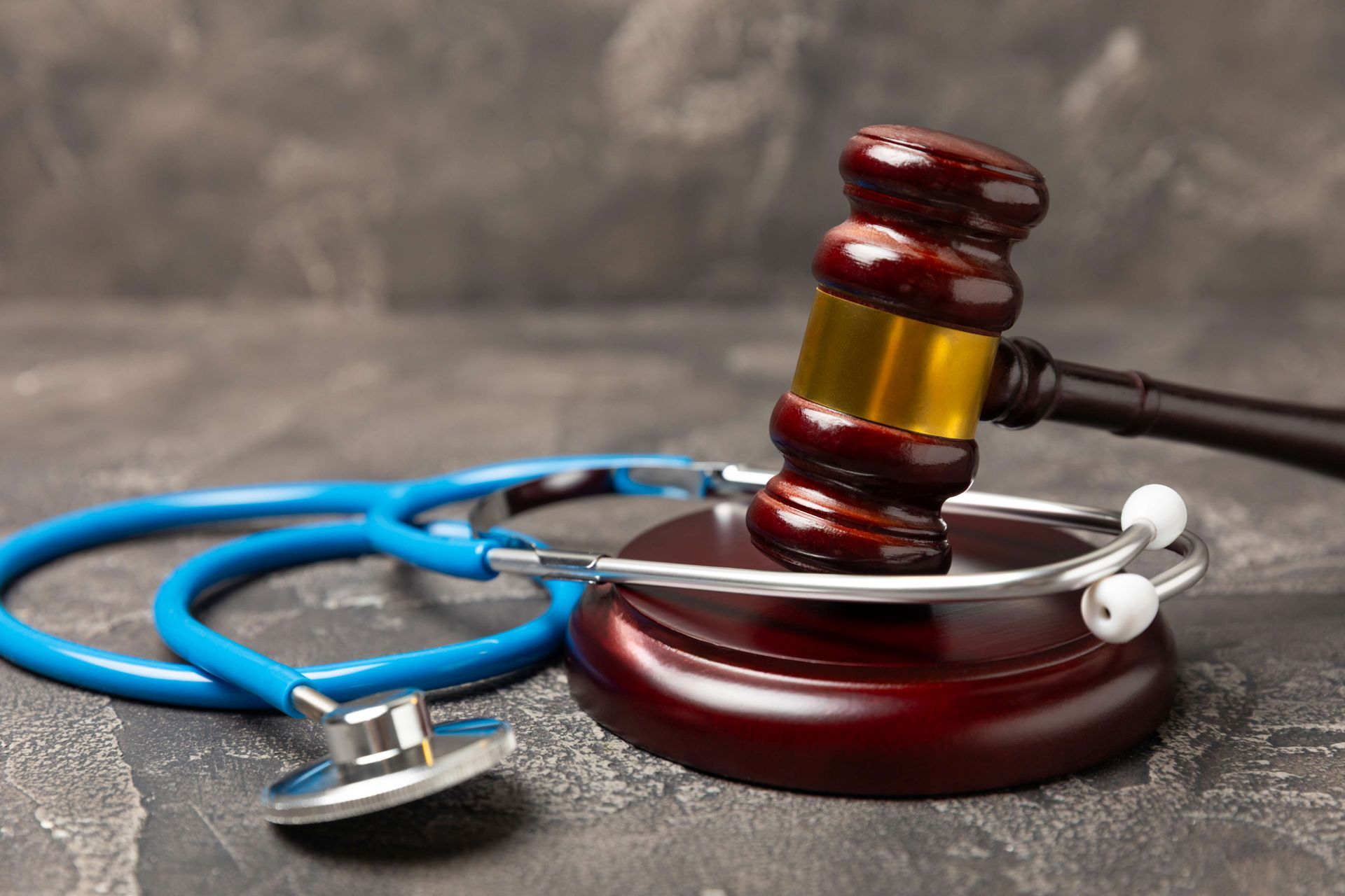 Judge’s gavel resting on a sound block beside a blue stethoscope on a textured surface.