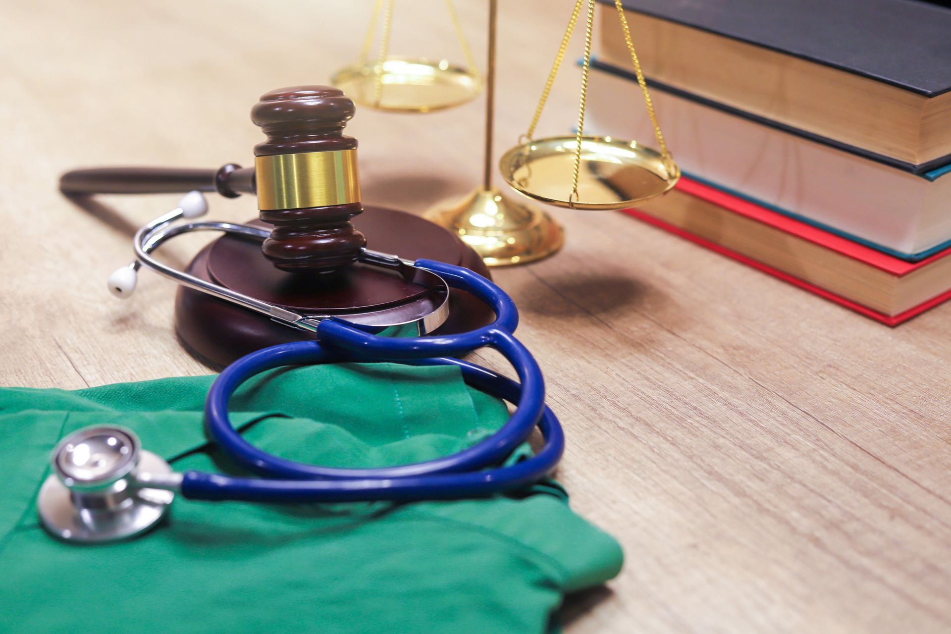 Gavel, scales of justice, stethoscope, books, and scrubs on a wooden surface, representing medical law.