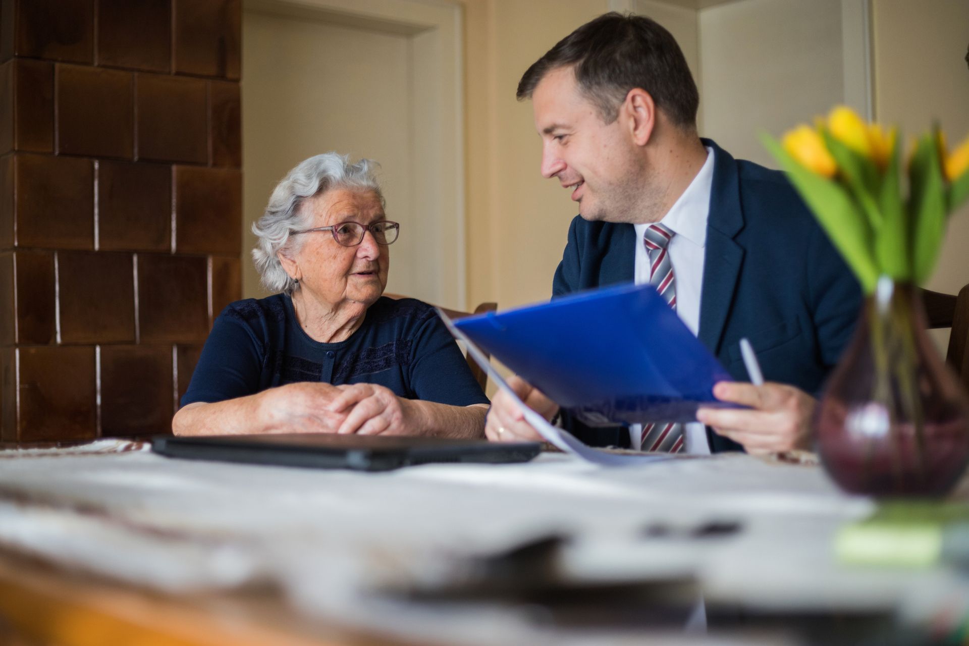 Man in suit reviews papers with elderly woman at a table indoors. Man in suit reviews papers with elderly woman at a table indoors.