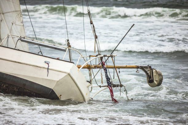 A small sailboat capsized in rough water, partially submerged.