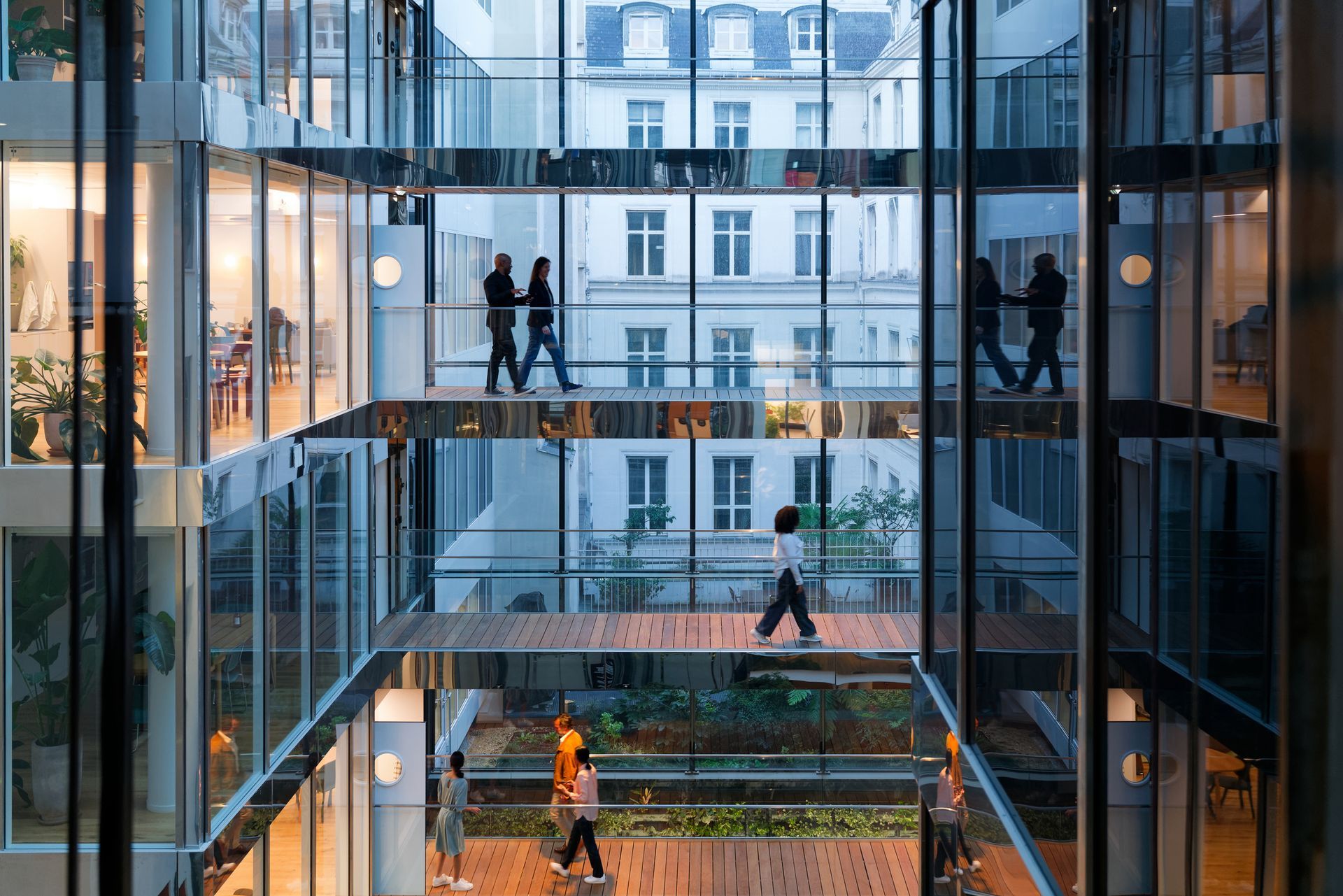 People walking in a modern multi-story office building with glass walls and bridges, view of a traditional building outside.