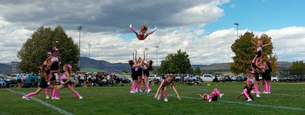 Cheerleader in red uniform performs a backbend on a green and red football field.