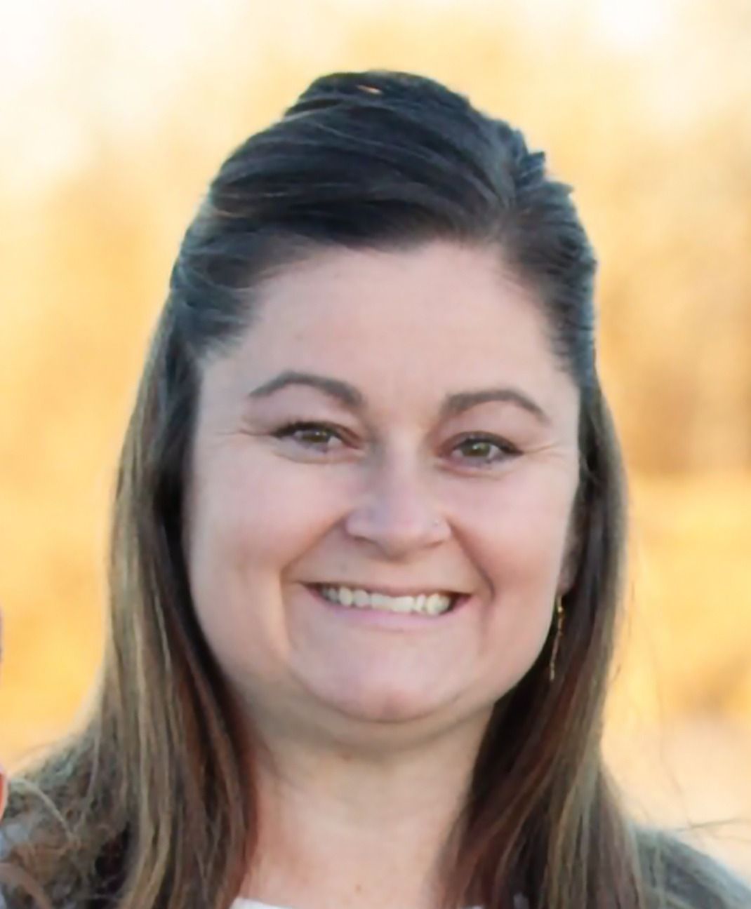 Man with crossed arms on a football field. He is wearing a blue polo shirt, khaki pants, and has a serious expression.
