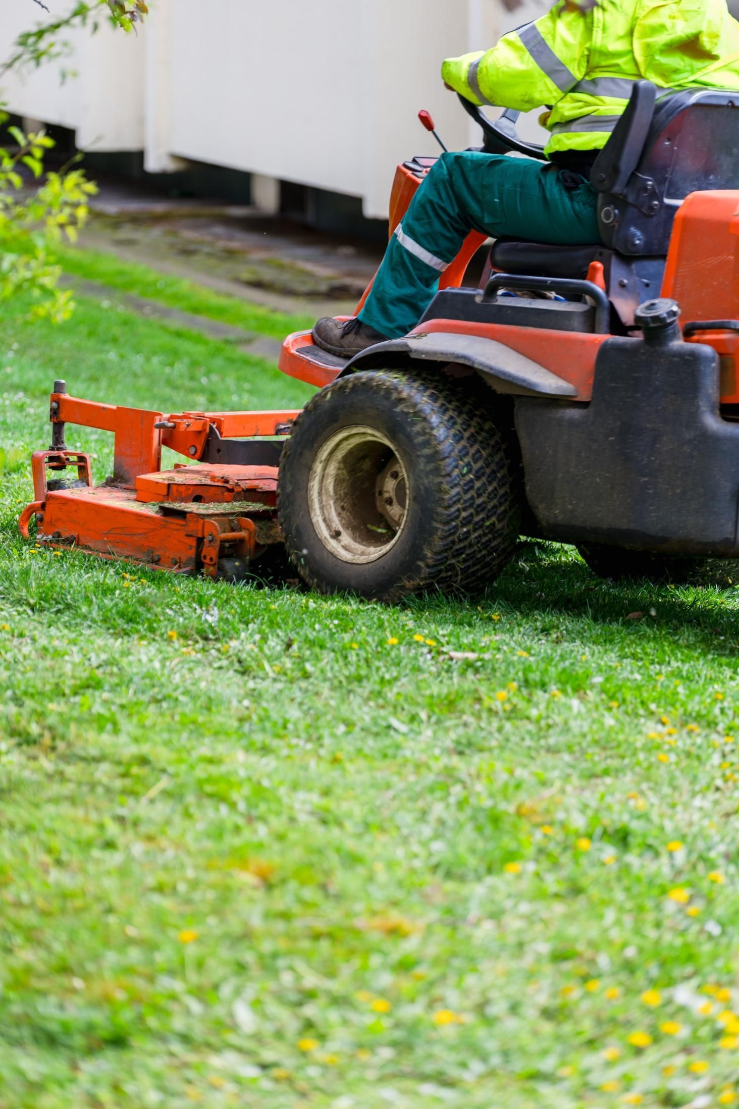 Person in safety vest driving an orange riding lawnmower cutting grass in a yard.