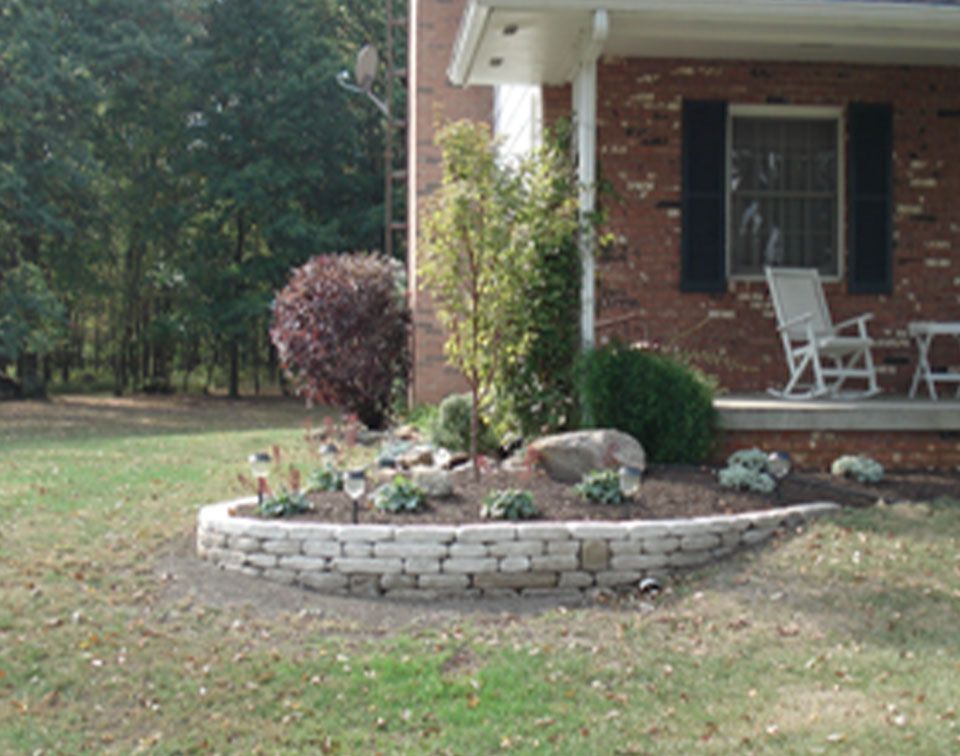 Brick home with a small stone retaining wall garden bed filled with plants and shrubs.
