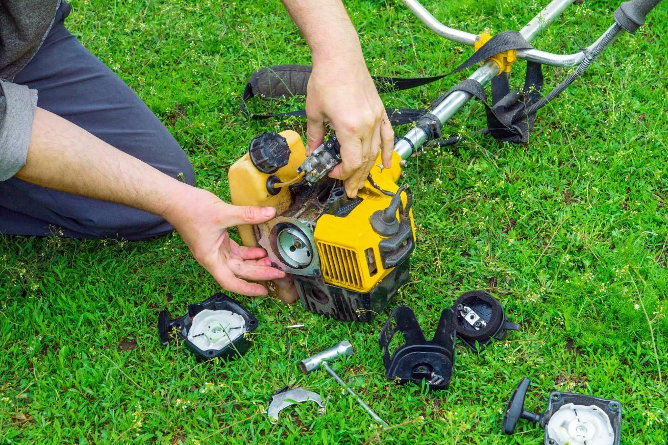 Person disassembling a yellow and black weed wacker on green grass.