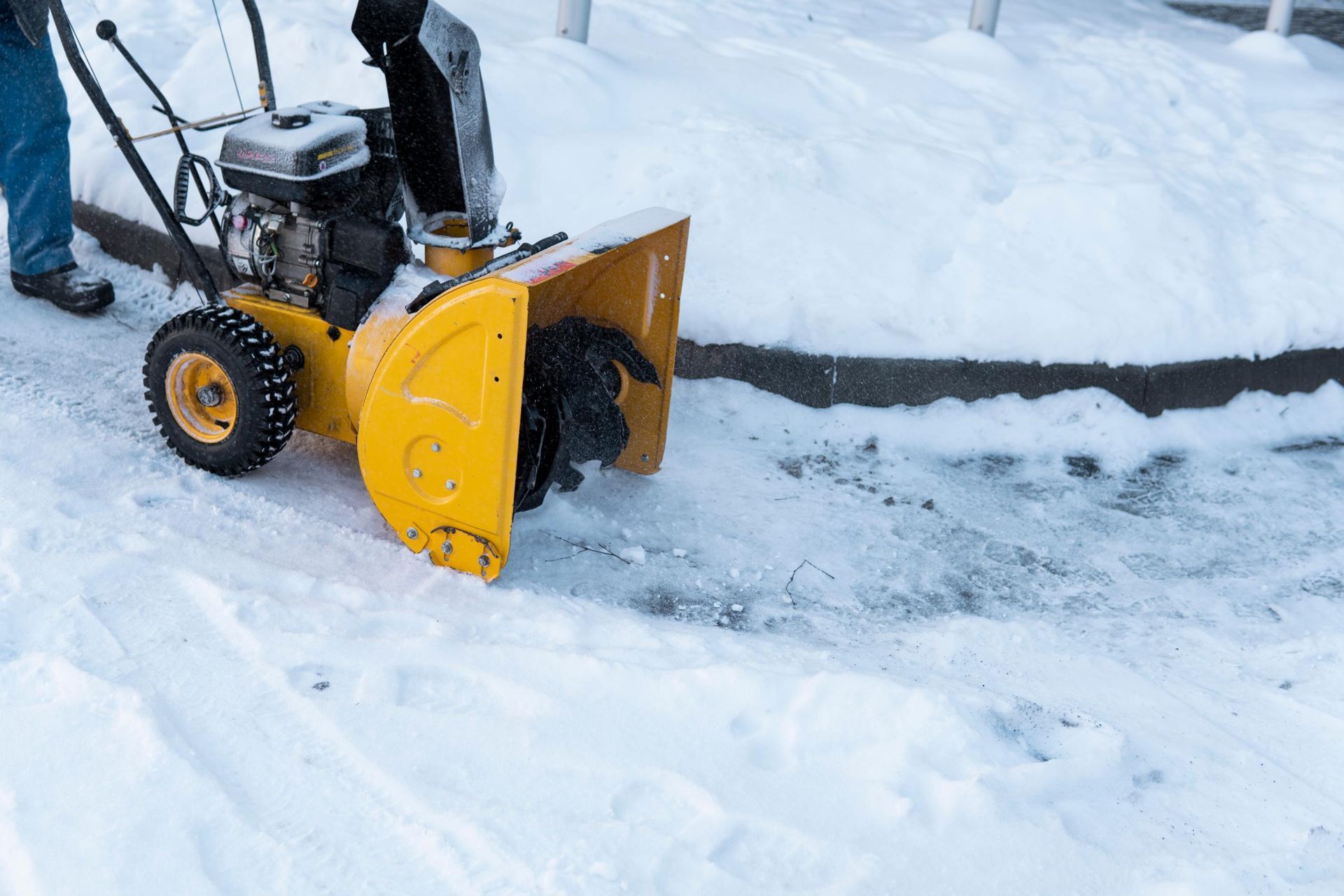 Yellow snowblower clearing snow on a sidewalk.