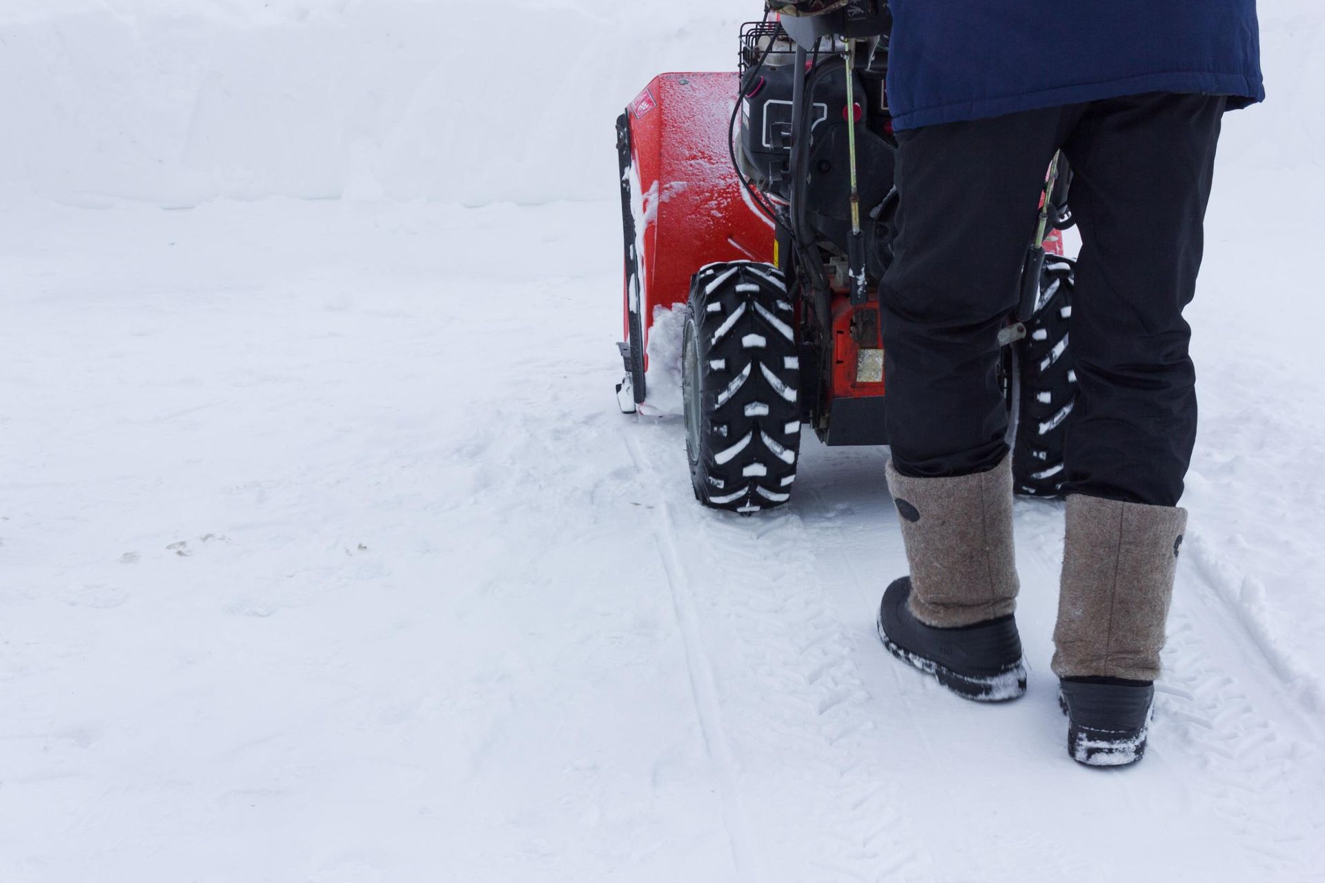 Person using a red snowblower to clear a snow-covered path.