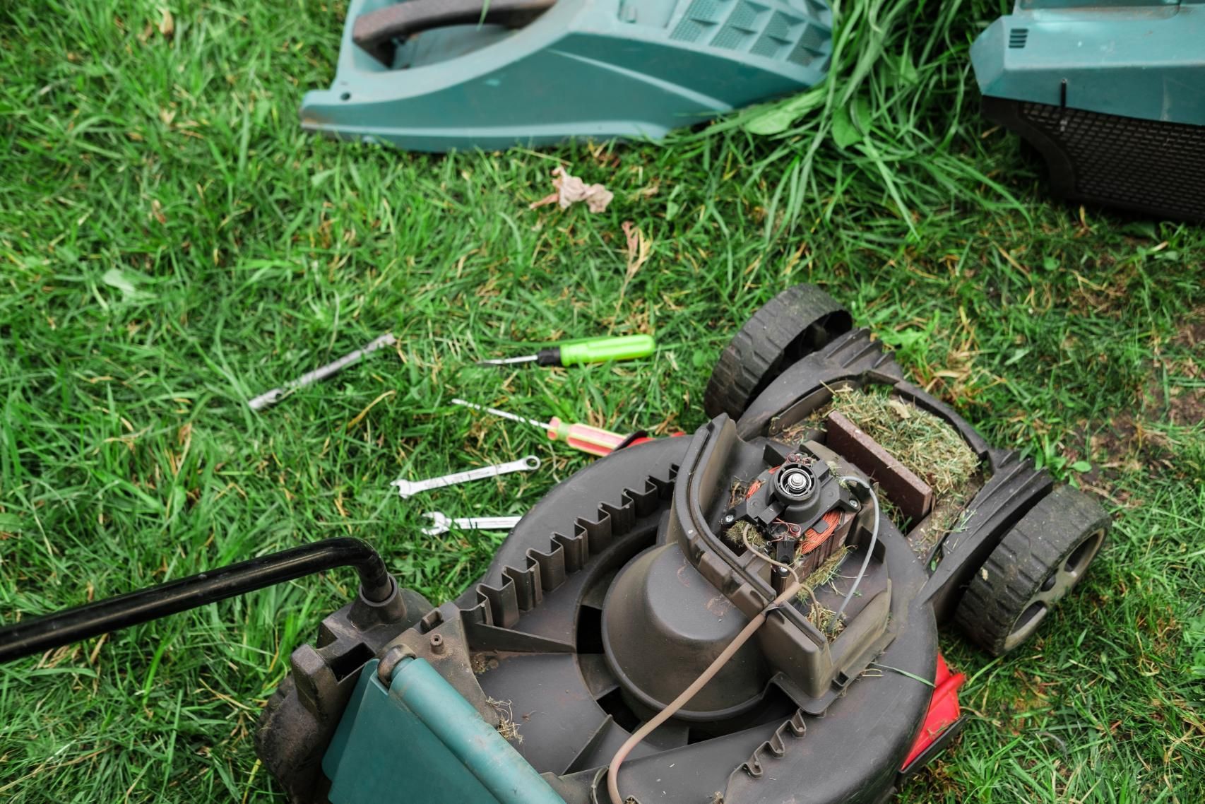 Lawnmower disassembled on grass with tools scattered nearby.