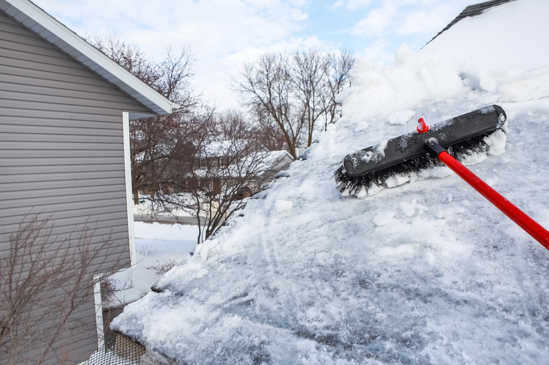 Removing snow from a roof with a long-handled brush on a winter day.