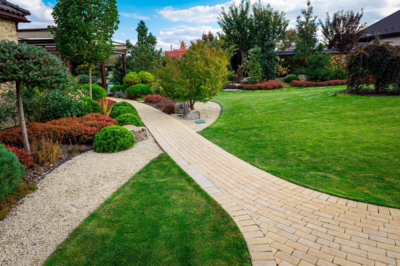 Brick pathway winds through landscaped garden with trees, shrubs, and green lawn.