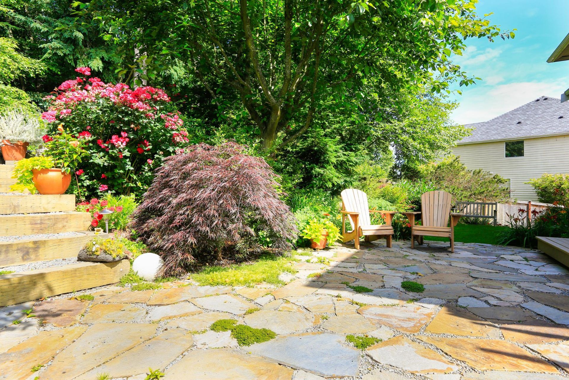 Stone patio with wooden chairs, surrounded by lush greenery and flowers.