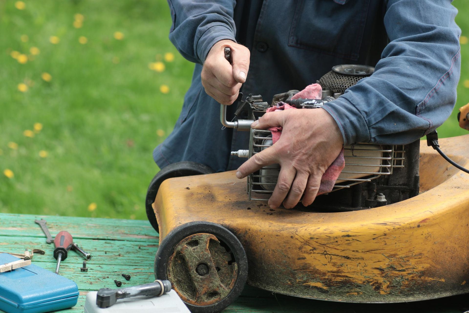 Person repairing a yellow lawnmower engine outdoors with tools on a green table.