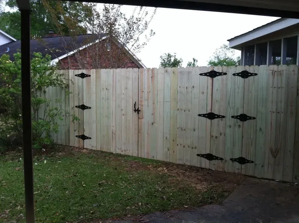 A wooden fence with a gate and a house in the background