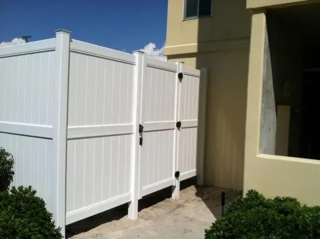 A white fence with a gate is next to a house.