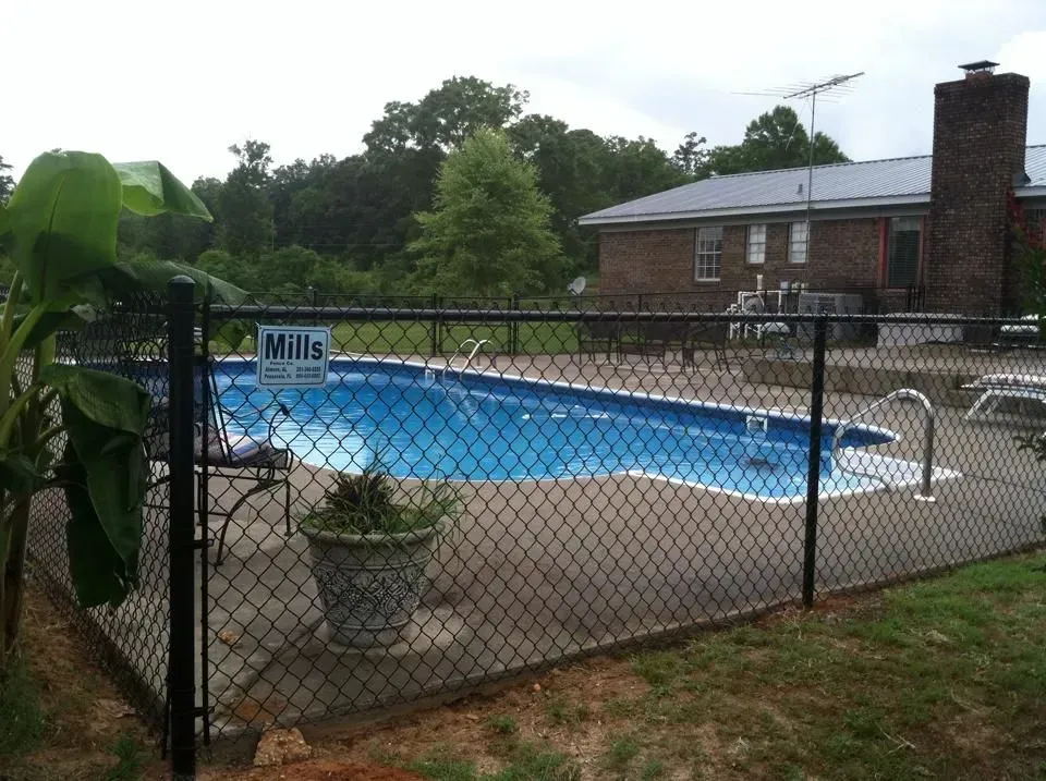 A chain link fence surrounds a swimming pool with a mills sign on it