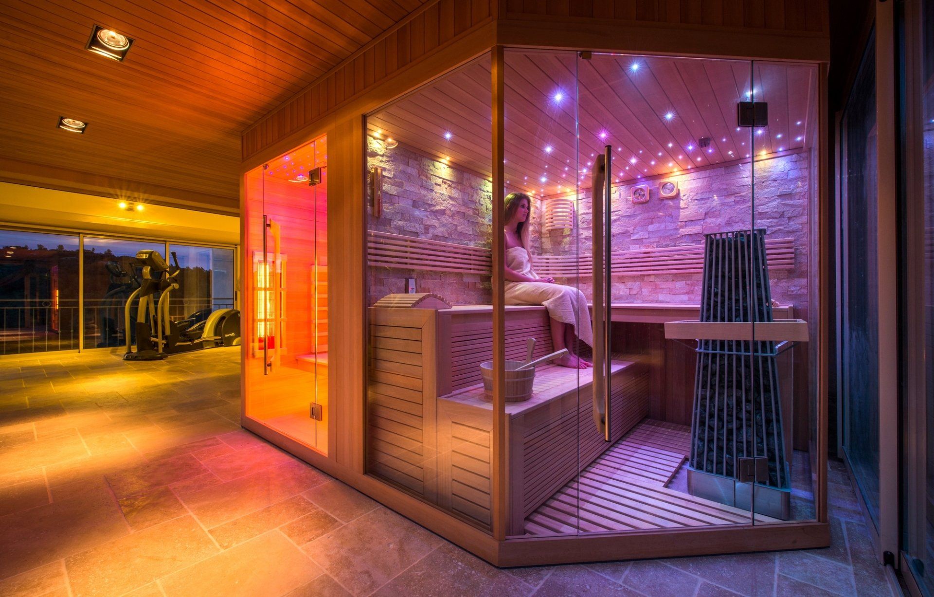 Une femme est assise dans un sauna en verre avec des lumières violettes.
