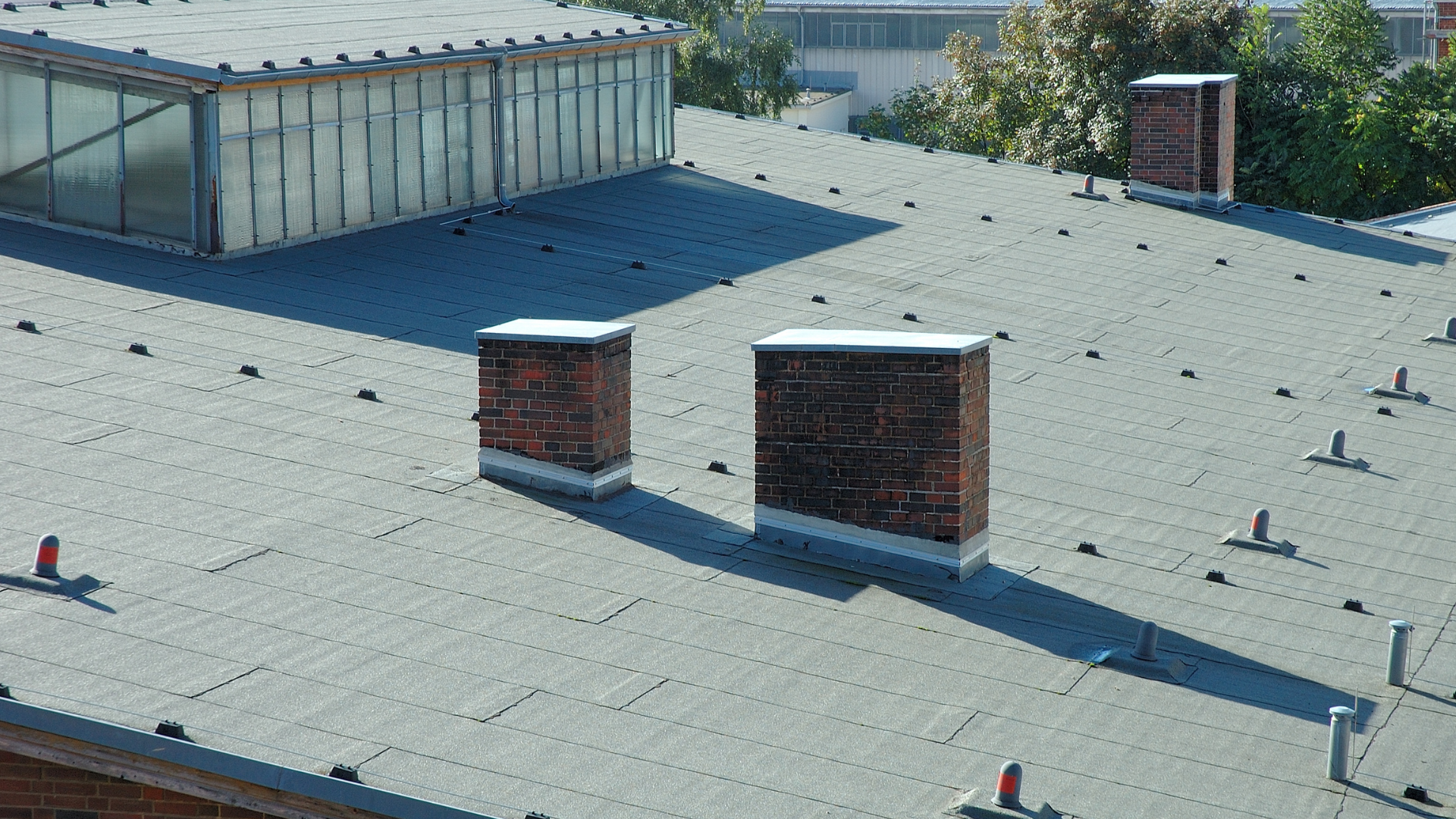 A roof with two chimneys on it and a building in the background